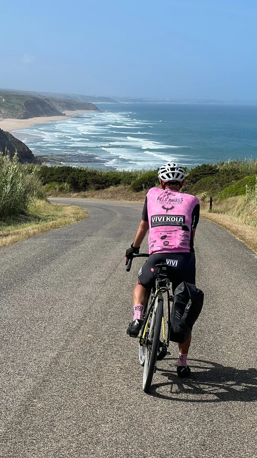 Hills Angels Radfahrer im pinken Teamtrikot auf einer Strasse mit Blick auf das Meer